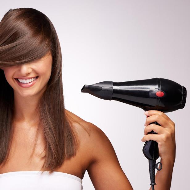 Eine Frau fönt sich die Haare vor weißem Hintergrund