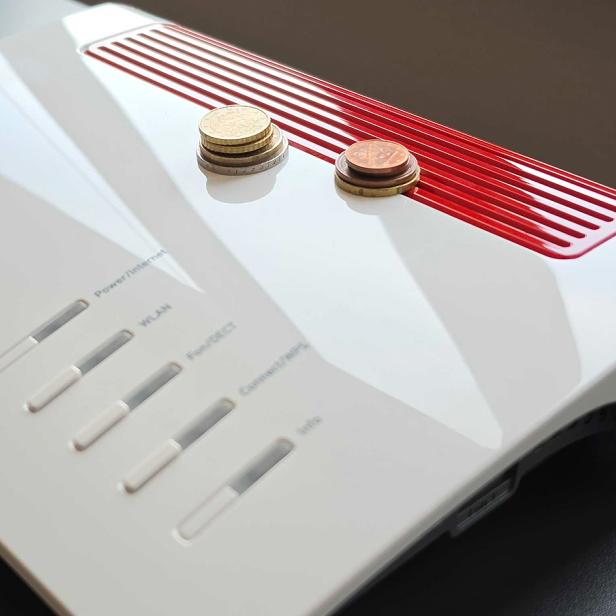 Mehrere Münzen liegen auf einem weißen Router mit roten Lüftungsschlitzen.