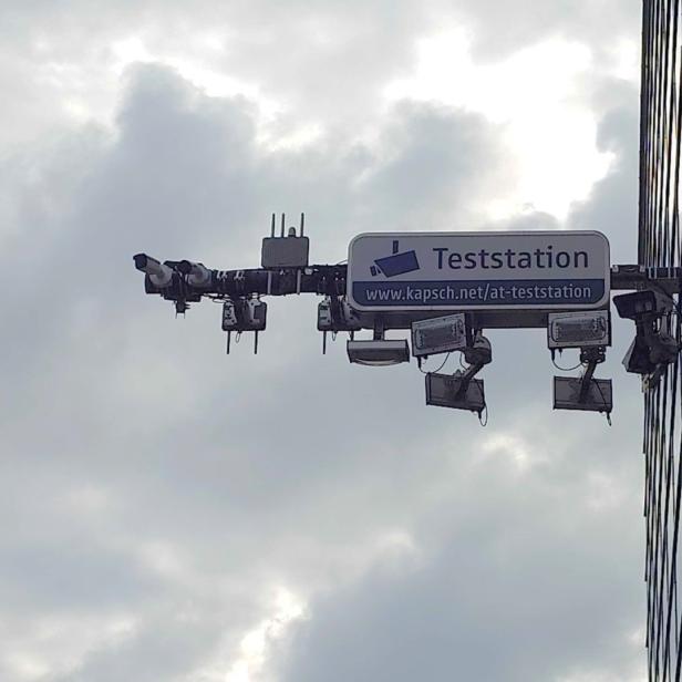 Mehrere Überwachungskameras und Scheinwerfer an einem Gebäude mit Schild „Teststation“.