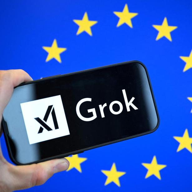 Eine Hand hält ein Smartphone mit dem Grok-Logo vor einem Hintergrund mit gelben Sternen auf blauem Grund.