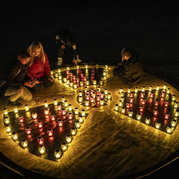Menschen zünden Kerzen auf einem großen gelben Symbol für Radioaktivität an, das aus vielen kleinen Lichtern besteht.