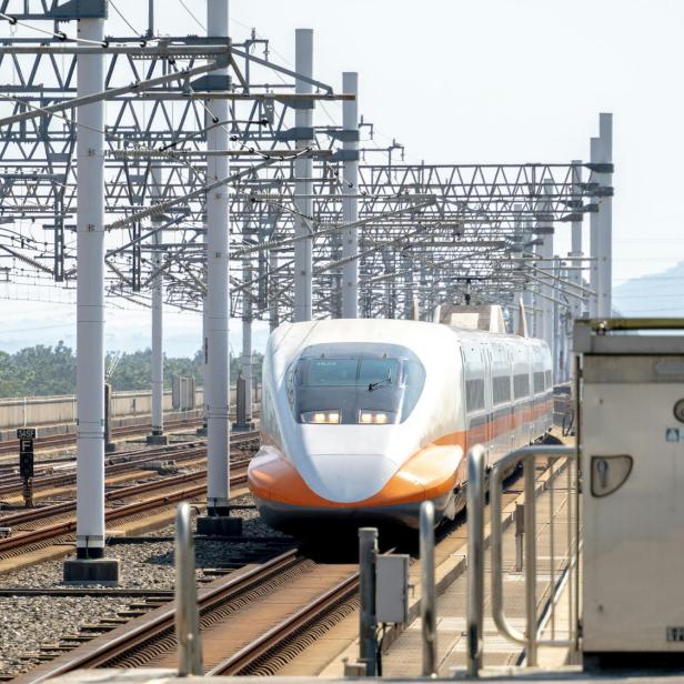 Ein Hochgeschwindigkeitszug fährt auf einer erhöhten Bahnstrecke unter Stromleitungen.
