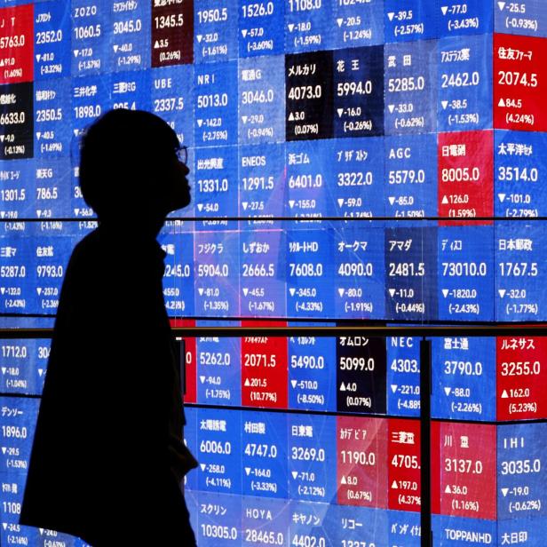 Eine Person steht vor einer großen digitalen Tafel mit zahlreichen Aktienkursen und Finanzdaten in Blau und Rot (Symbolbild)