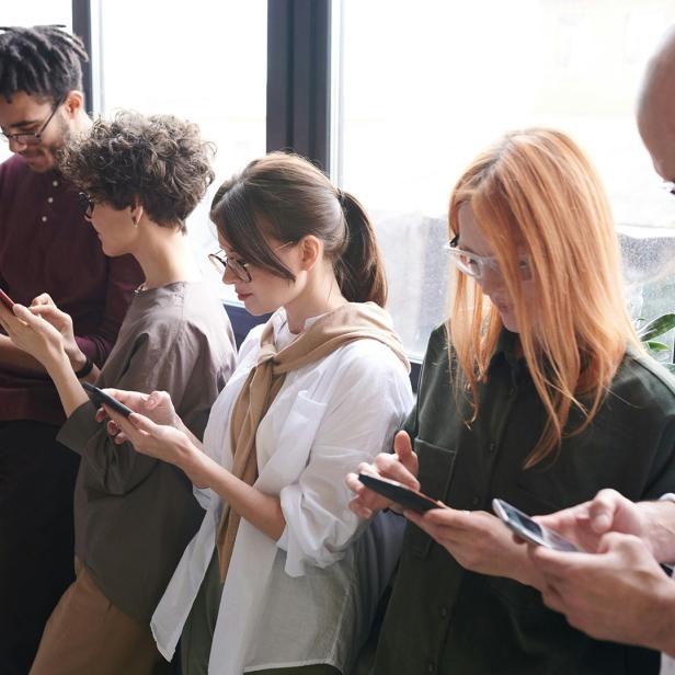 Mehrere Menschen stehen nebeneinander und tippen konzentriert auf ihre Smartphones.