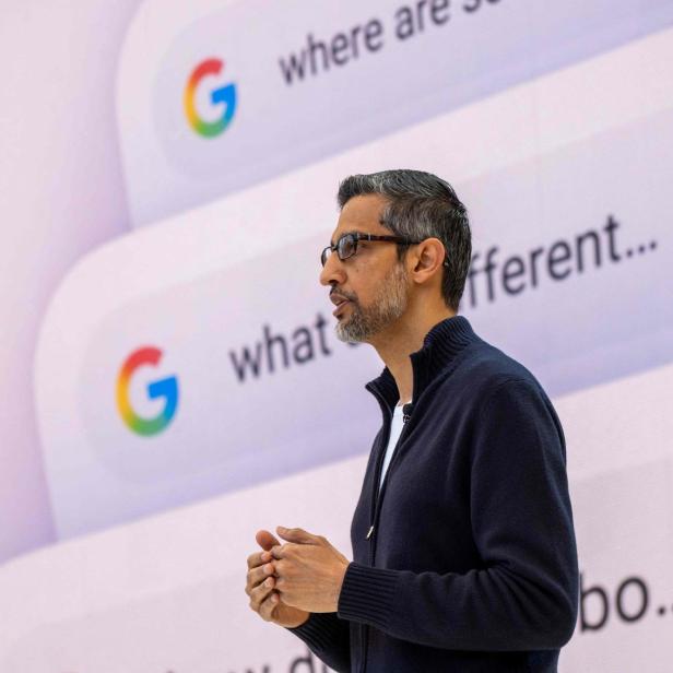 Ein Mann spricht vor einer großen Leinwand mit Google-Suchanfragen und buntem Mikrofon-Symbol.