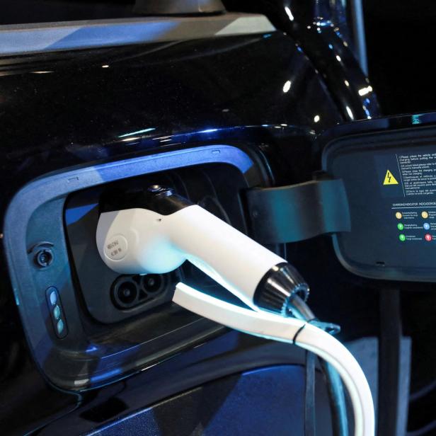 Ein weißes Ladekabel ist an ein schwarzes Elektroauto angeschlossen, die Ladeklappe ist geöffnet.