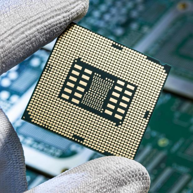 Hand mit Handschuh hält einen Mikrochip über einer Leiterplatte.