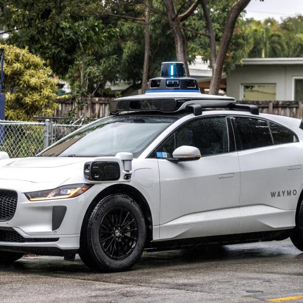 Weißes autonomes Elektroauto mit Sensoren und Kameras auf dem Dach und an den Seiten, mit der Aufschrift „Waymo“.