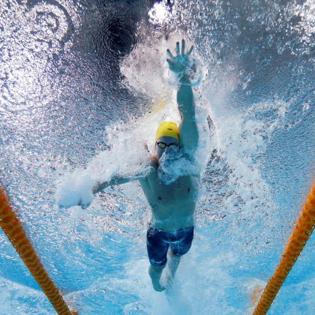 Ein Schwimmer mit gelber Badekappe schwimmt kraulend zwischen zwei gelben Bahnleinen unter Wasser.