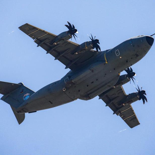 Ein graues Militärflugzeug mit Propellern ist vor blauem Himmel zu sehen.