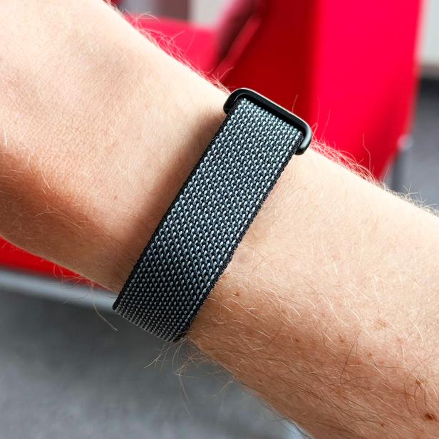 Graues Fitbit Air am Arm mit rotem Sessel im Hintergrund