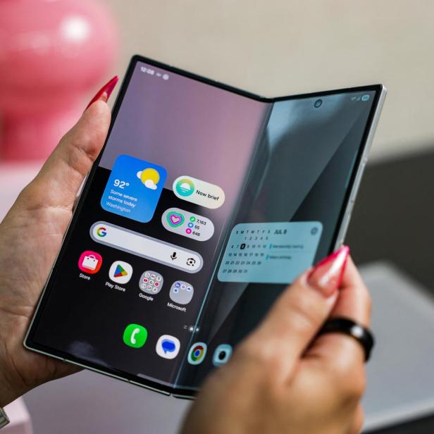 Eine Person hält ein faltbares Smartphone mit Wetter- und Kalender-Widgets in der Hand.