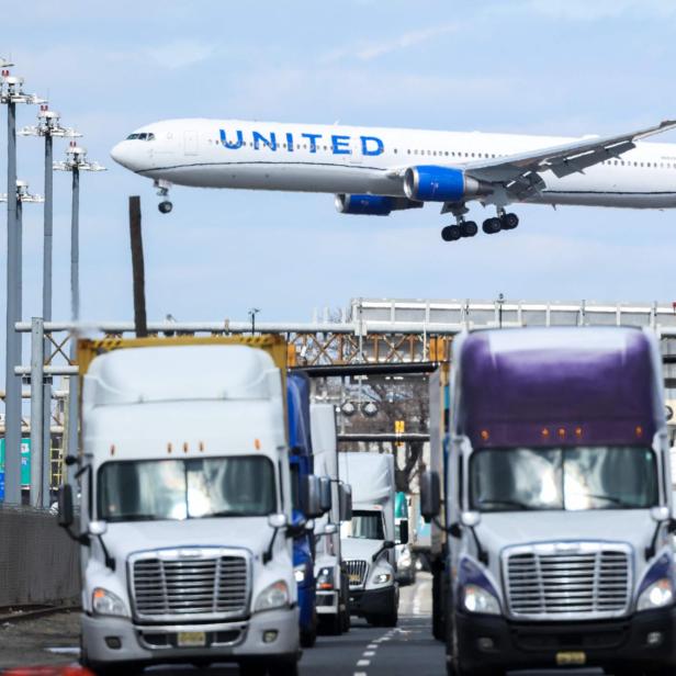 Ein Flugzeug fliegt niedrig über einer belebten Straße mit mehreren Lastwagen und Verkehrsschildern.
