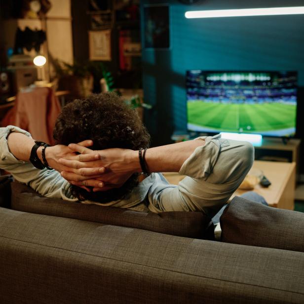 Ein Mann sitzt auf dem Sofa vor dem Fernseher.