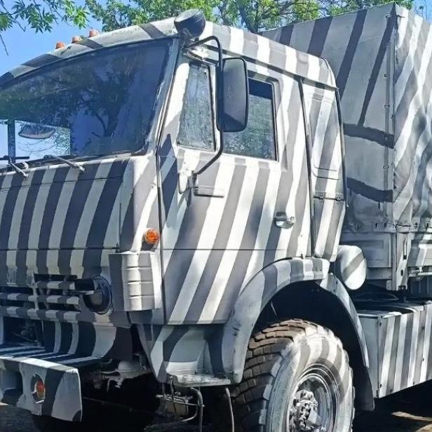 Russischer Lastwagen mit auffälligem Zebramuster steht auf einem Feldweg neben Bäumen.