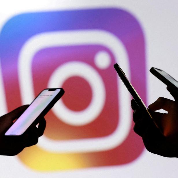 Drei Hände halten Smartphones vor einem großen, unscharfen Instagram-Logo mit Farbverlauf im Hintergrund.