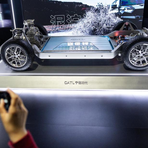 Ein elektrisches Fahrzeug-Chassis mit sichtbarem Batteriepaket und Reifen wird auf einer Messe ausgestellt.