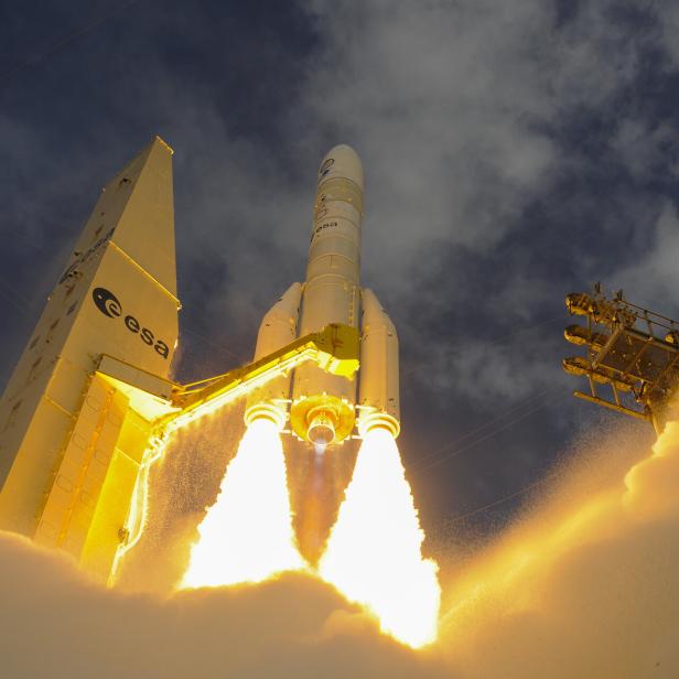 Eine Ariane-Rakete der ESA startet mit leuchtenden Feststoffboostern und erzeugt dichte Rauch- und Feuersäulen am Boden.