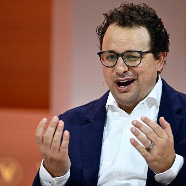 Anthropic-CEO Dario Amodei spricht gestikulierend vor einem orangefarbenen Hintergrund.