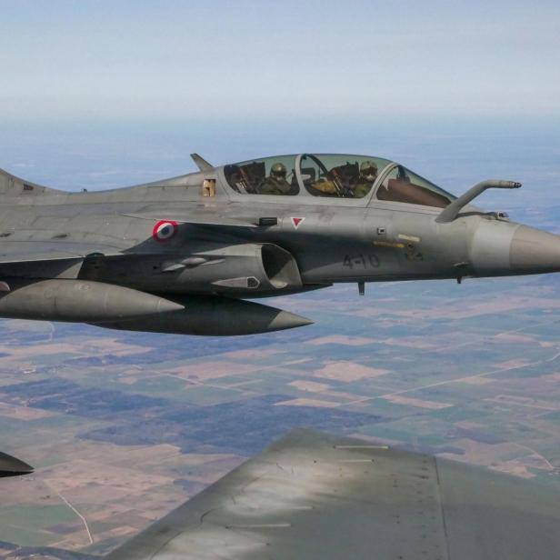 Kampfjet mit zwei Piloten im Cockpit fliegt über eine ländliche Landschaft.