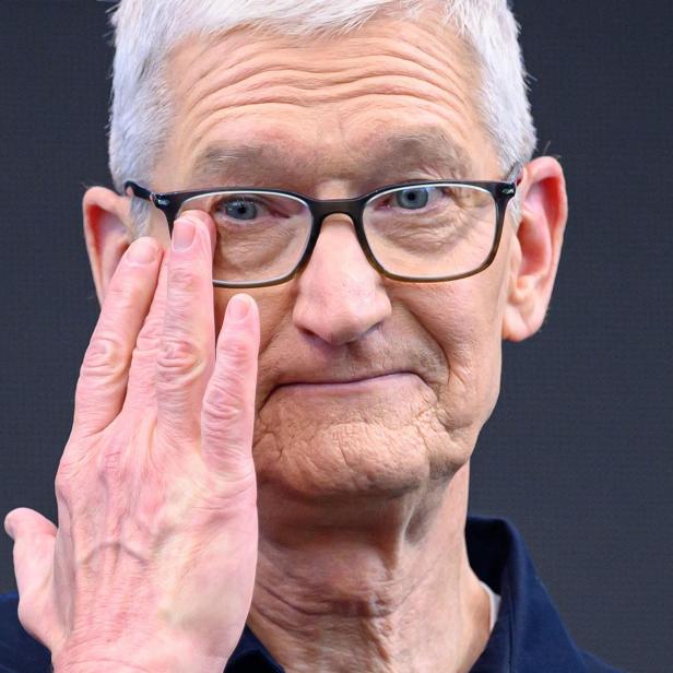 Ein älterer Mann mit Brille hebt die Hand an sein Gesicht und blickt nach vorne.