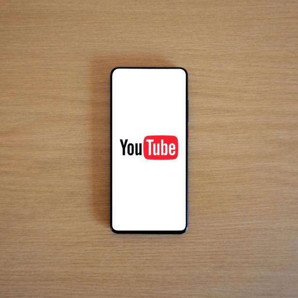Smartphone mit YouTube-Logo auf dem Bildschirm liegt auf einem Holztisch.