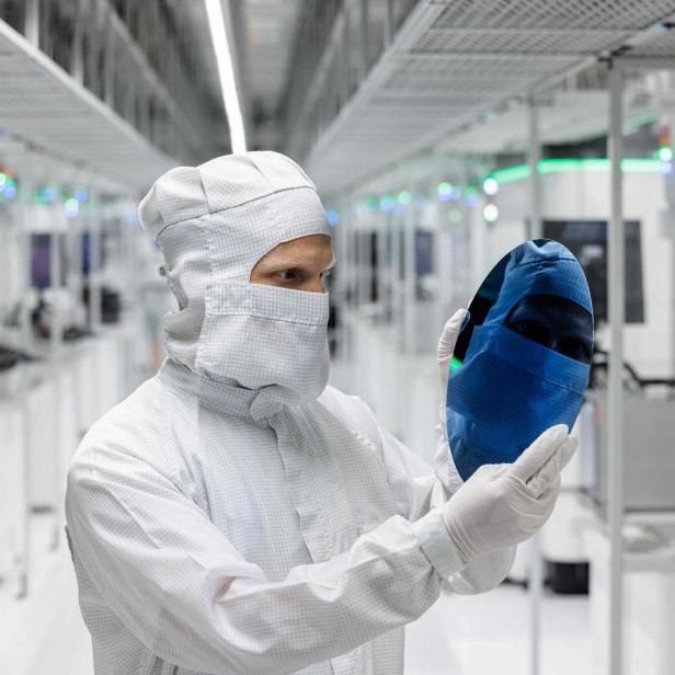 Eine Person im Reinraumanzug hält eine Siliziumscheibe in einer modernen Hightech-Fertigungsanlage.