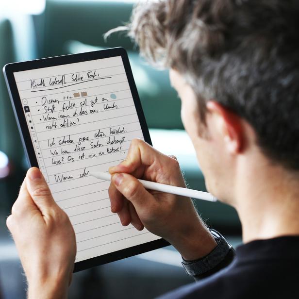 Eine Person schreibt mit einem Stift handschriftliche Notizen auf einem Tablet mit liniertem Bildschirm.