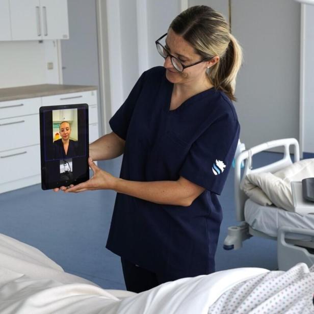 Pflegekraft zeigt per Tablet eine Video-Sprechstunde einem Patienten im Krankenhauszimmer.