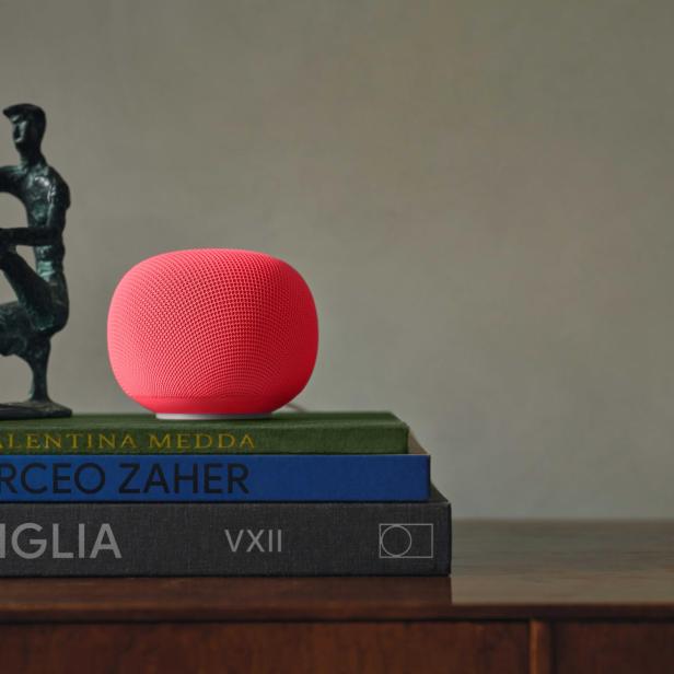 Eine rote Smart-Speaker-Kugel neben einer kleinen Skulptur auf gestapelten Büchern.