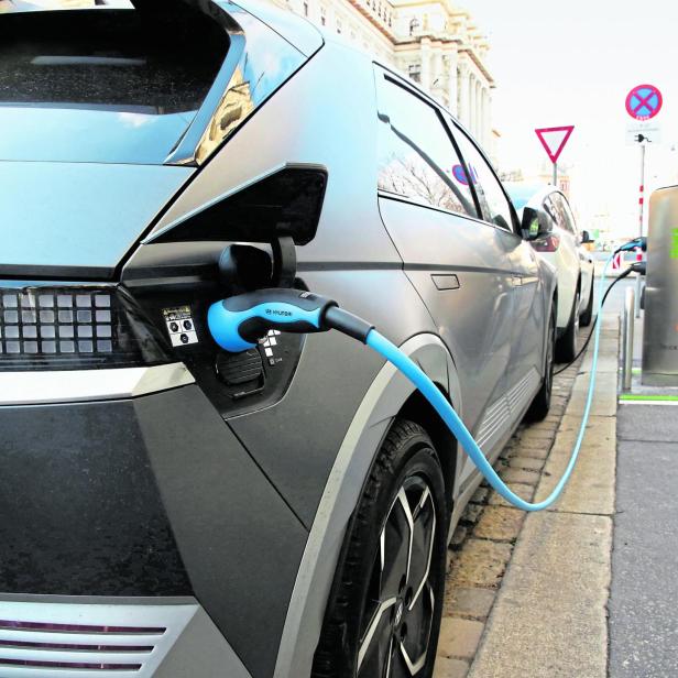 Graues Elektroauto lädt an einer Straßensäule am Bordstein.