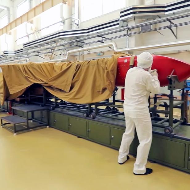Eine Rakete in einer Produktionshalle wird von einer Person überprüft.