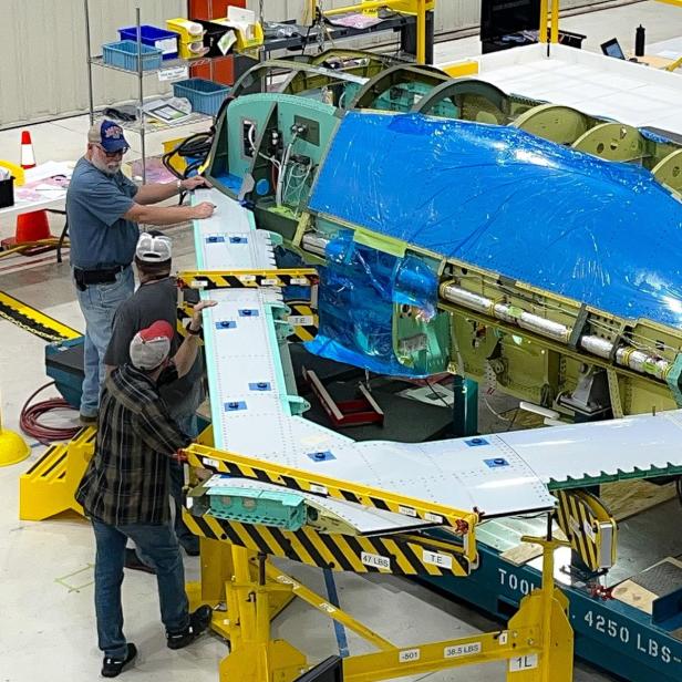 Techniker montieren Tragflächen an den X-65-Rumpf in der Werkhalle.