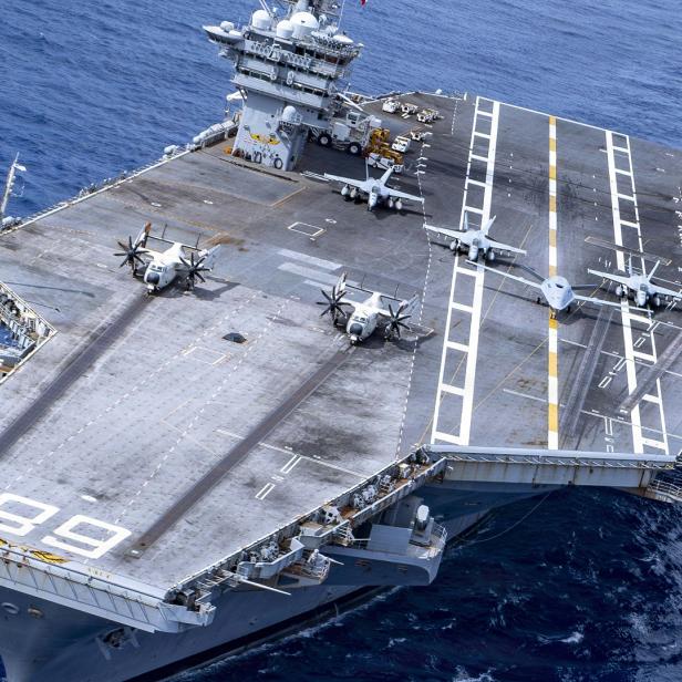 Ein Flugzeugträger der US Navy mit der Kennung 89 fährt auf dem offenen Meer, während mehrere Militärflugzeuge auf seinem Deck geparkt sind.