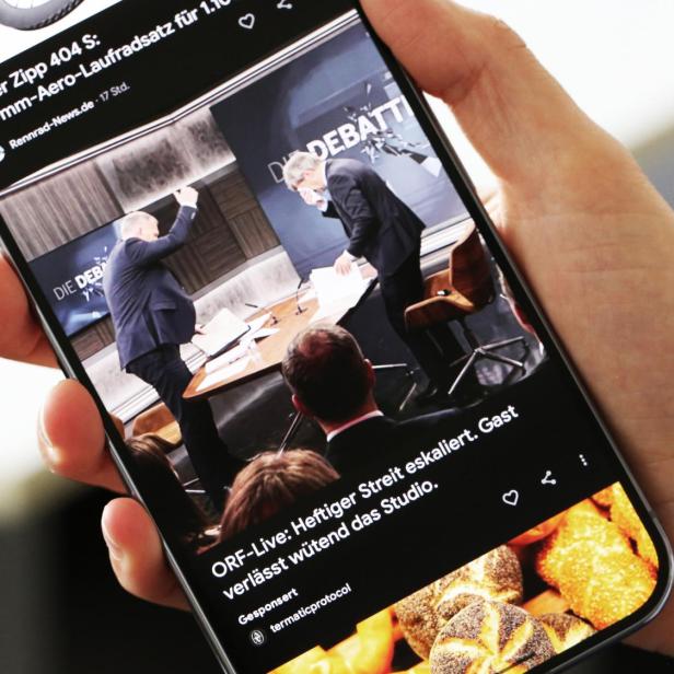 Eine Hand hält ein Smartphone, das einen eskalierenden Streit in einer ORF-Live-Debatte zeigt, bei der ein Gast wütend das Studio verlässt.