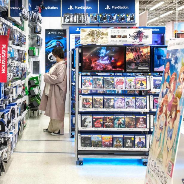 Kundin in einem PlayStation-Regalgang prüft Spiele und Zubehör im Elektronikmarkt.