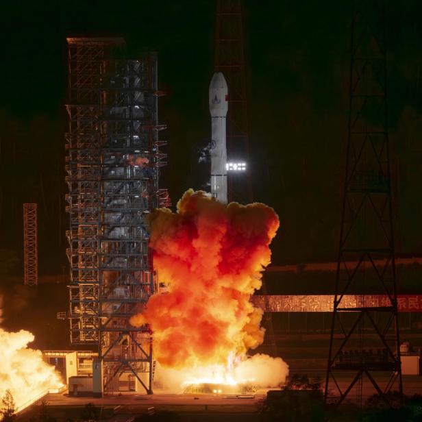 Rakete startet nachts auf der Startrampe, umgeben von grellen Flammen und dichtem Rauch.