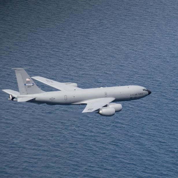 Ein graues Tankflugzeug fliegt über dem blauen Meer