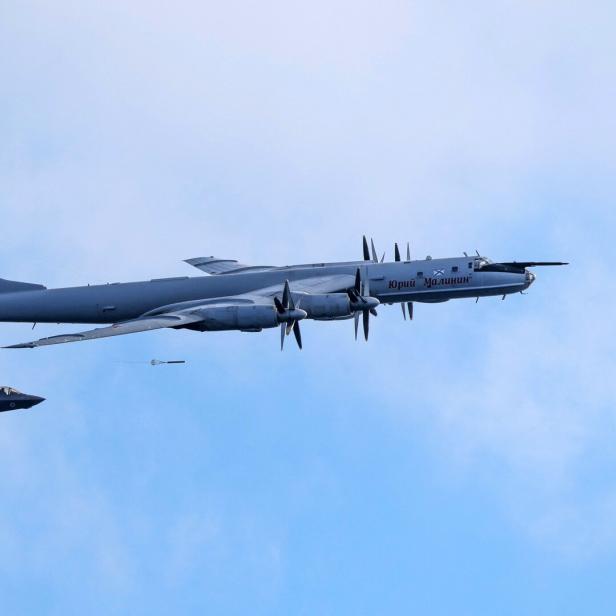 Ein russischer Tupolew Tu-142-Aufklärer fliegt vor einem F-35-Kampfjet am blauen Himmel.