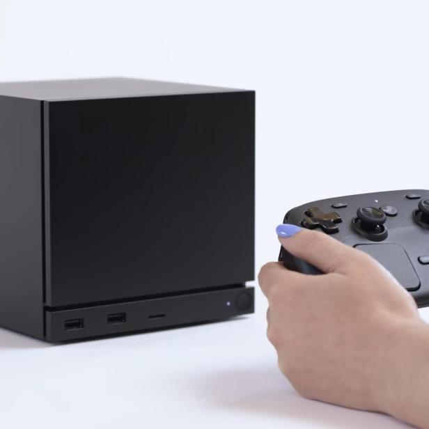 Schwarzer Gaming-PC steht im Hintergrund, eine Frau hält einen Controller im Vordergrund