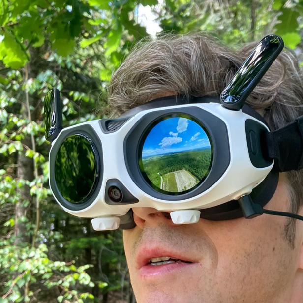 Mann trägt VR-Drohnenbrille im Wald, auf dem Display ist eine Landschaft zu sehen.