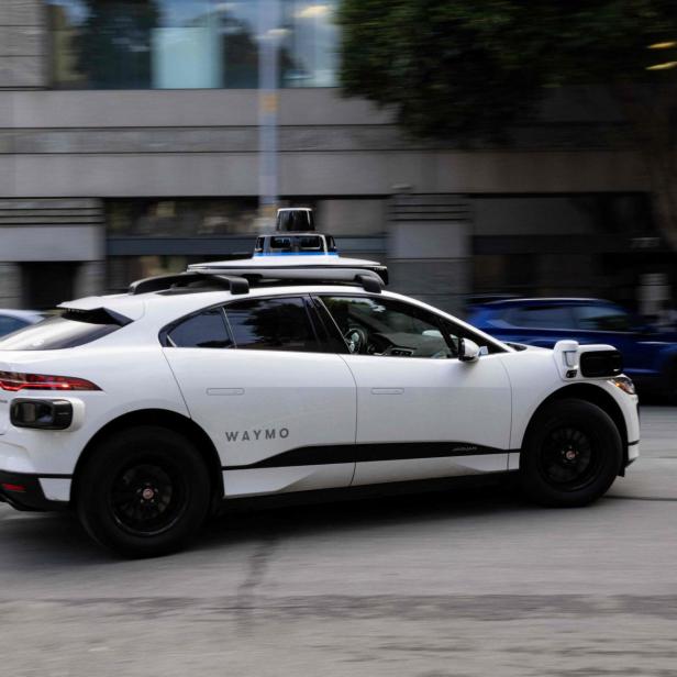 Weißes Waymo-Selbstfahrauto fährt durch eine Stadtstraße.