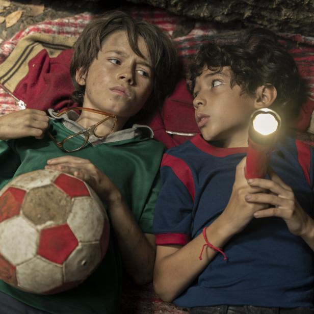 Zwei Jungen liegen auf einer Decke, einer hält einen Fußball und der andere eine Taschenlampe.