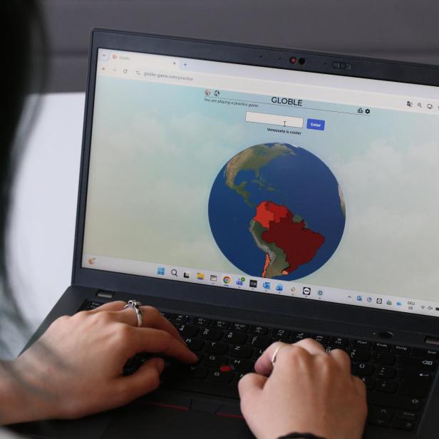 Person tippt auf einem Laptop ein Geografie-Spiel mit einer farbigen Weltkarte.