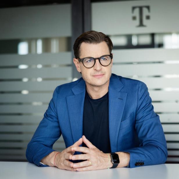 Thomas Kicker sitzt im Büro vor einer Glastür mit Telekom-Logo.