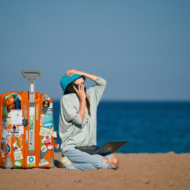 Frau mit Koffer und Handy am Strand