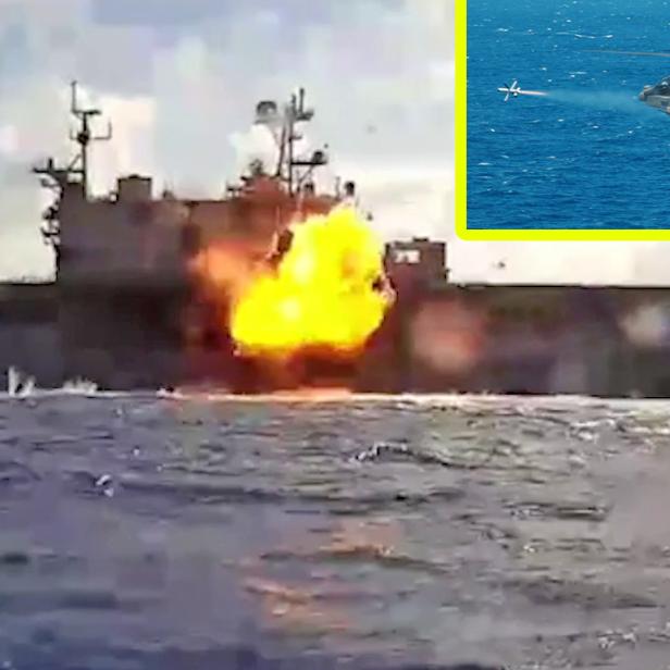 Eine Explosion ist mittig auf einem Schiff zu sehen. Rechts oben feuert ein Kampfhubschrauber eine Rakete ab.