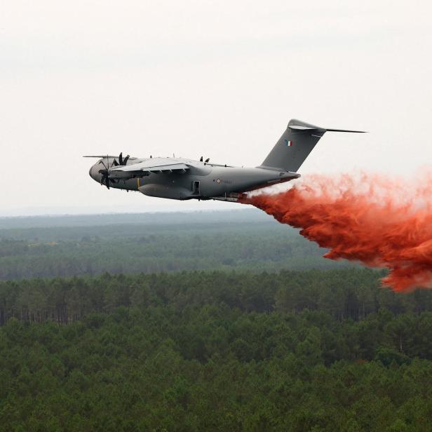 Graues Löschflugzeug wirft rote Brandbekämpfungsflüssigkeit über einem Wald ab.