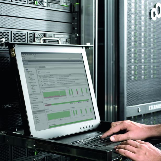 Ein Mann arbeitet an einem Laptop vor einem ETERNUS CS Serverschrank.
