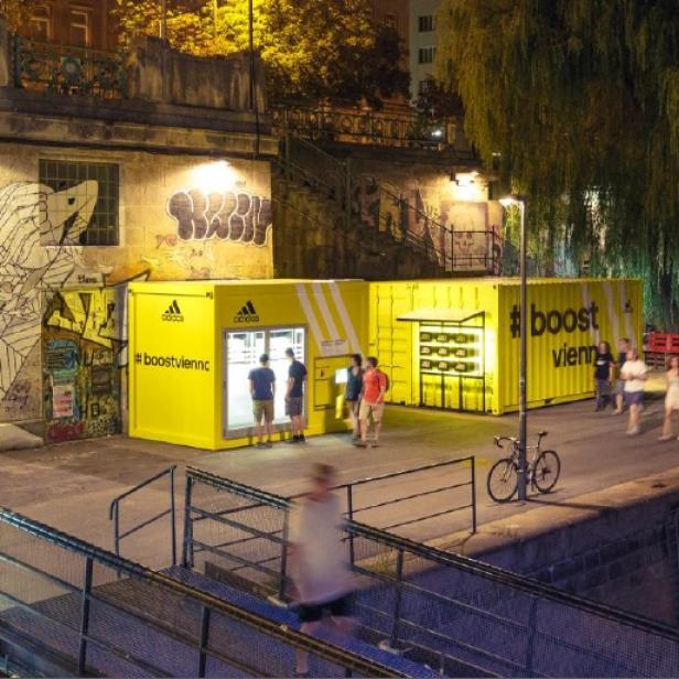 Gelbe Adidas-Container mit der Aufschrift „#boostvienna“ stehen an einem belebten Platz in Wien.